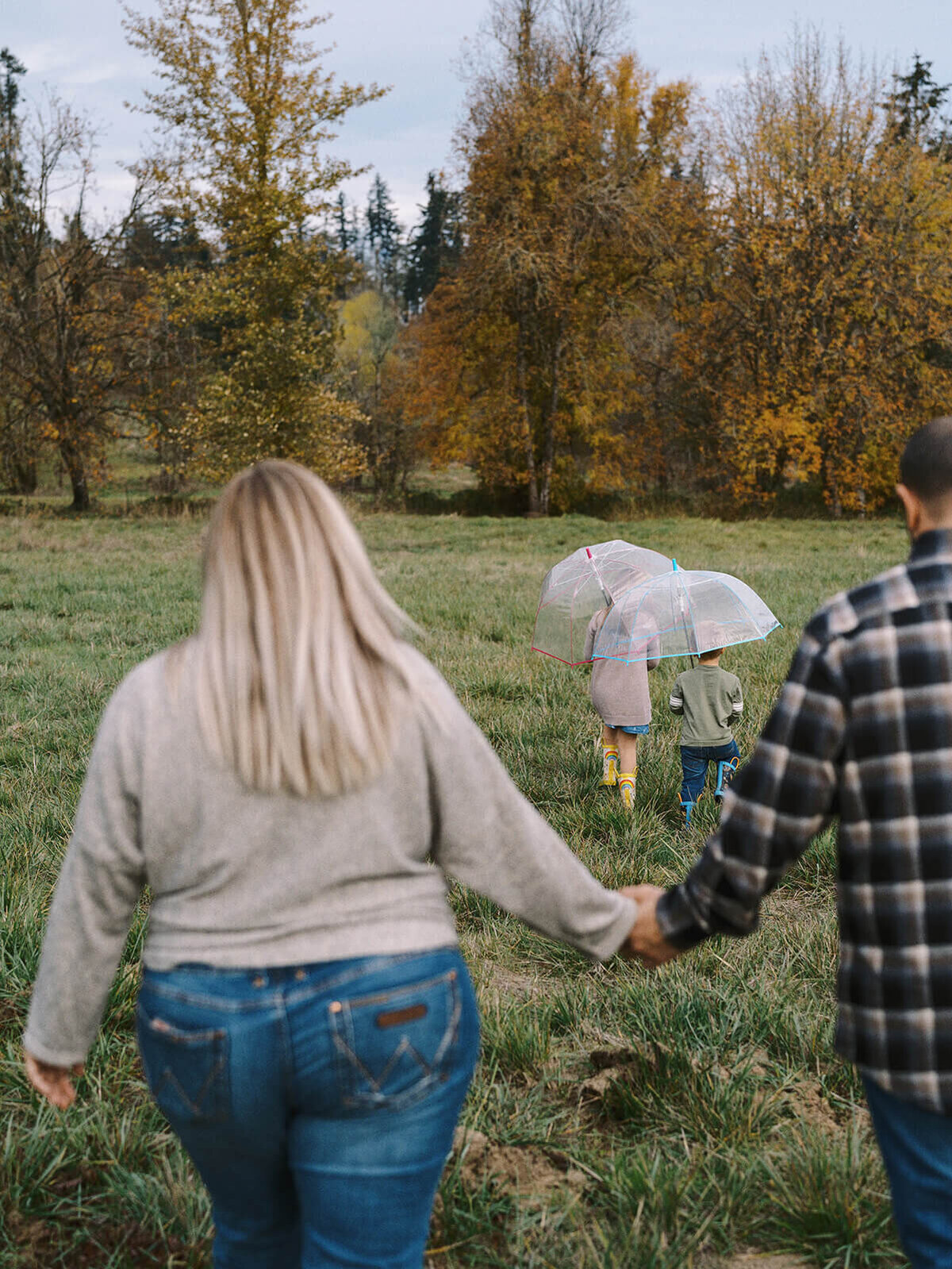 A man and woman holds hands with two children holding umbrellas in the background.