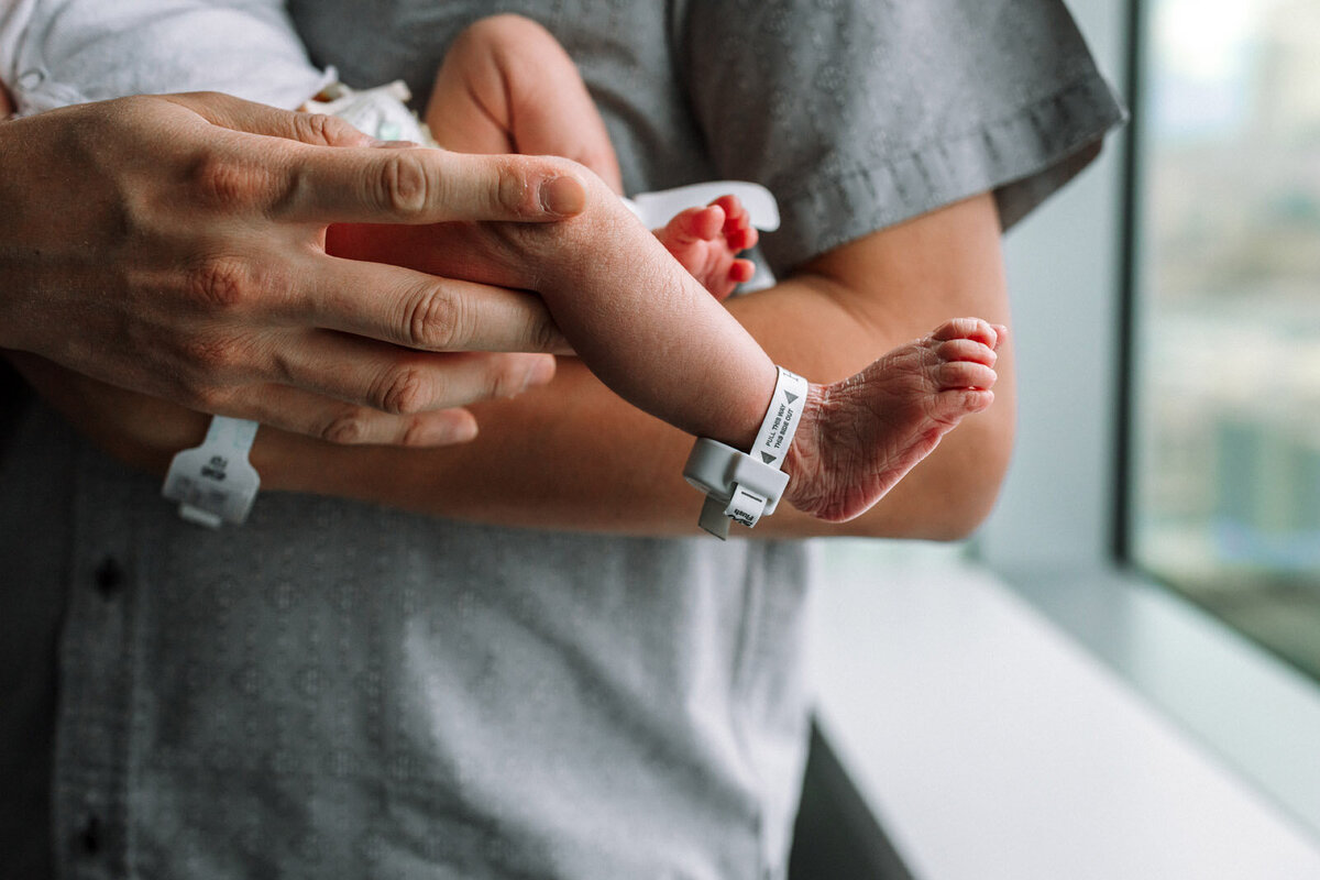 father's holding newborn with baby's leg extended with hospital anklet