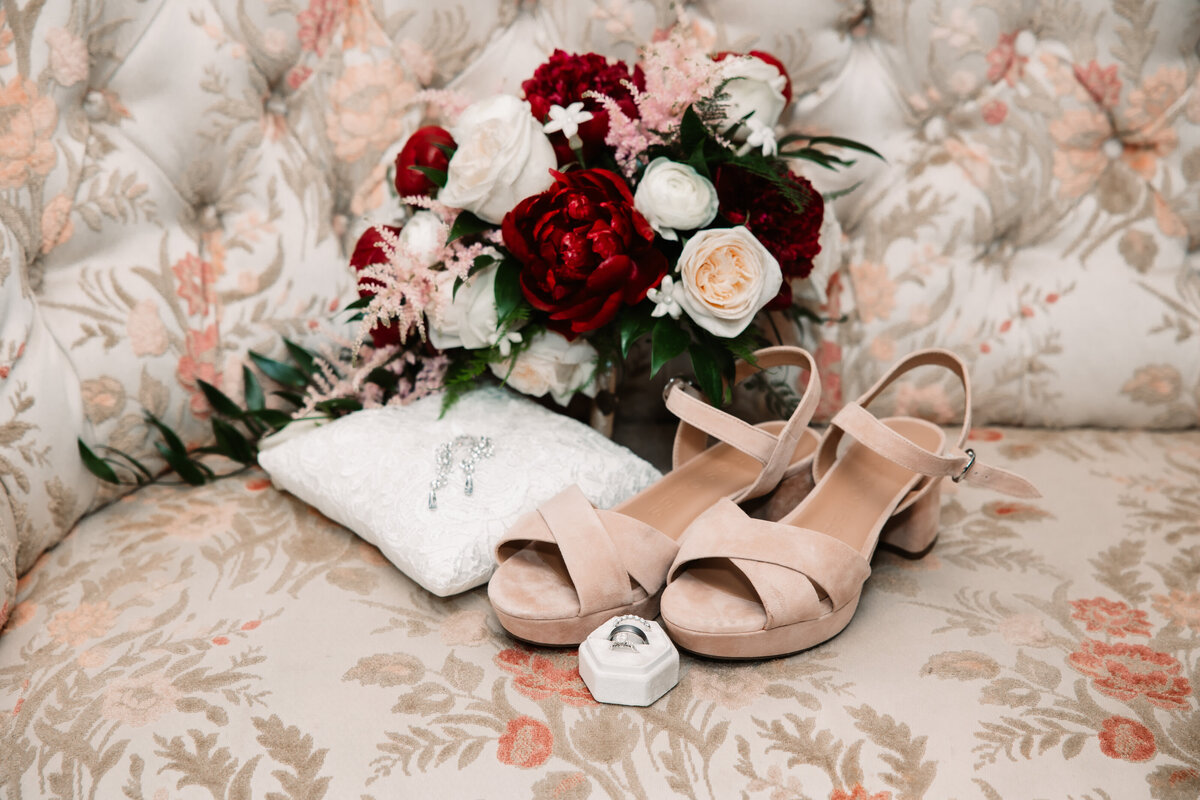 A bride's shoes, jewelry and bouquet sit on an antique couch