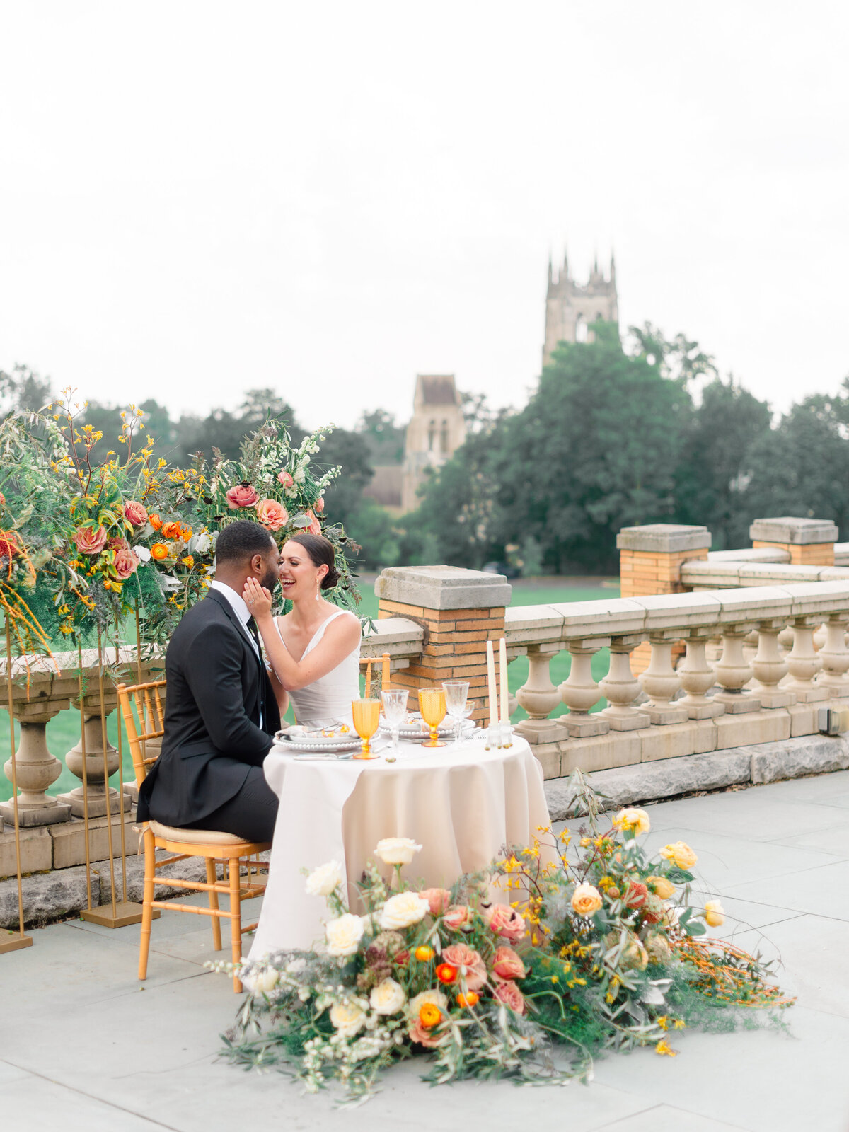 Romantic wedding editorial at Cairnwood Estate featuring an elegant sweetheart table overflowing with lush floral arrangements in warm summer tones. Captured by Philadelphia Fine Art Wedding Photographer Elizabeth Kane, this luxury outdoor reception scene blends timeless romance with historic East Coast charm, showcasing upscale wedding inspiration for refined couples.