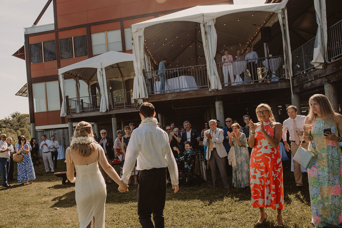 A wedding couple holding hands and walking into their reception as their guests cheer 