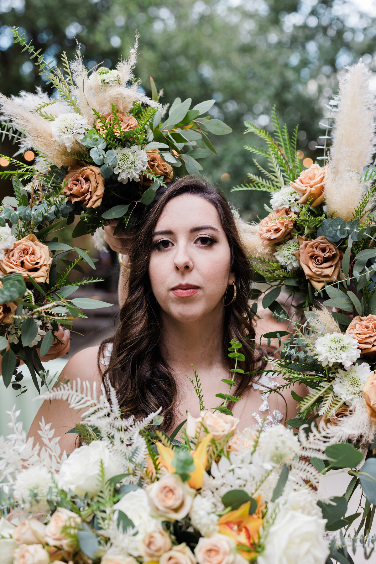 Portrait of a bride surrounded by a ring of bouquets after her wedding ceremony at The 4 Eleven in Fort Worth, Texas. The bride is wearing a sleeveless, white dress and all the bouquets are being held up by her wedding party out of frame.