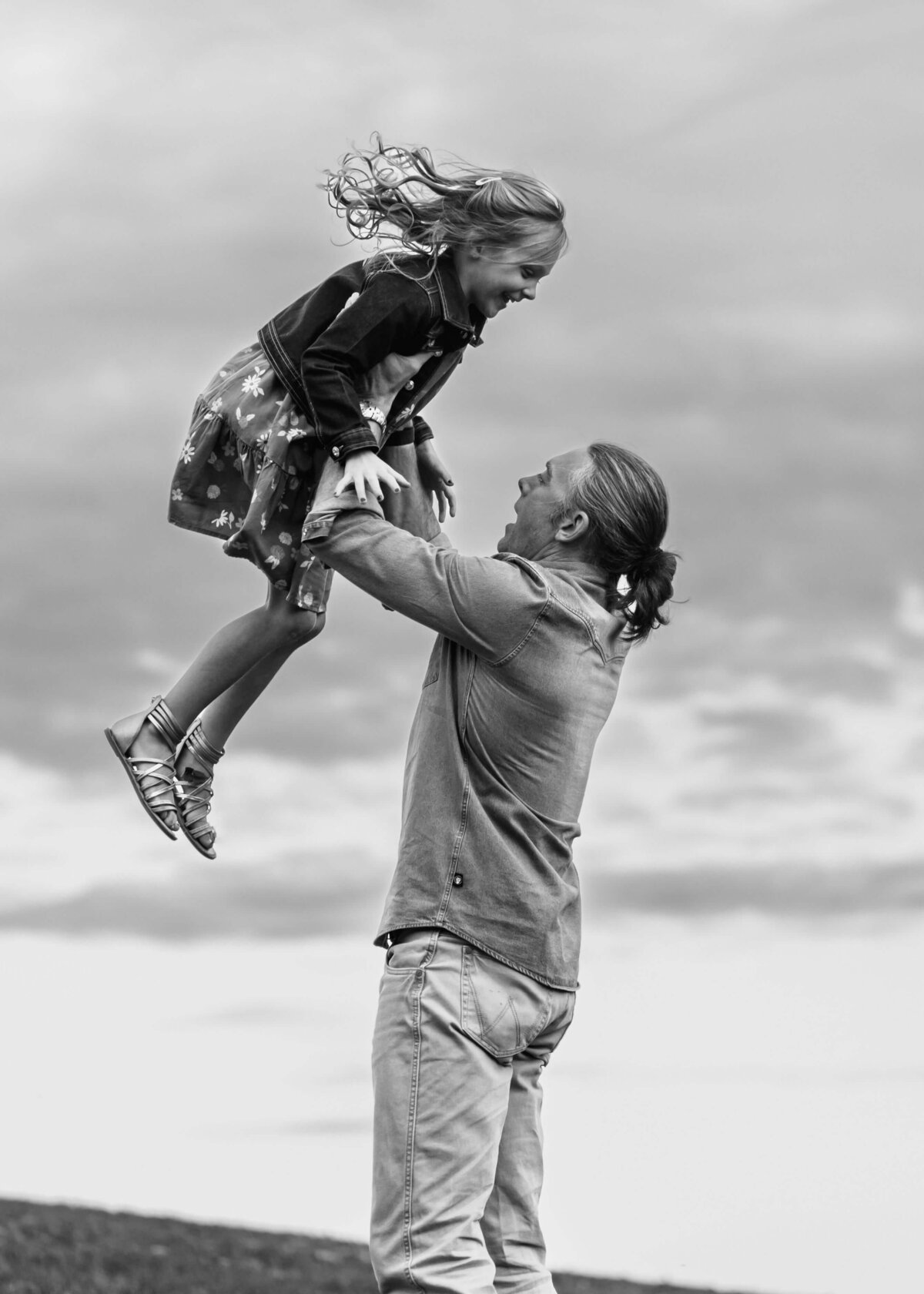 A man is lifting a little girl in the air as captured by a Pittsburgh family photographer.