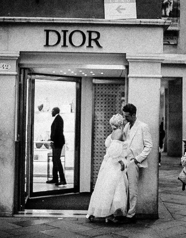 A candid moment of the couple in front of the Dior storefront, blending luxury and romance in their Venice engagement session.