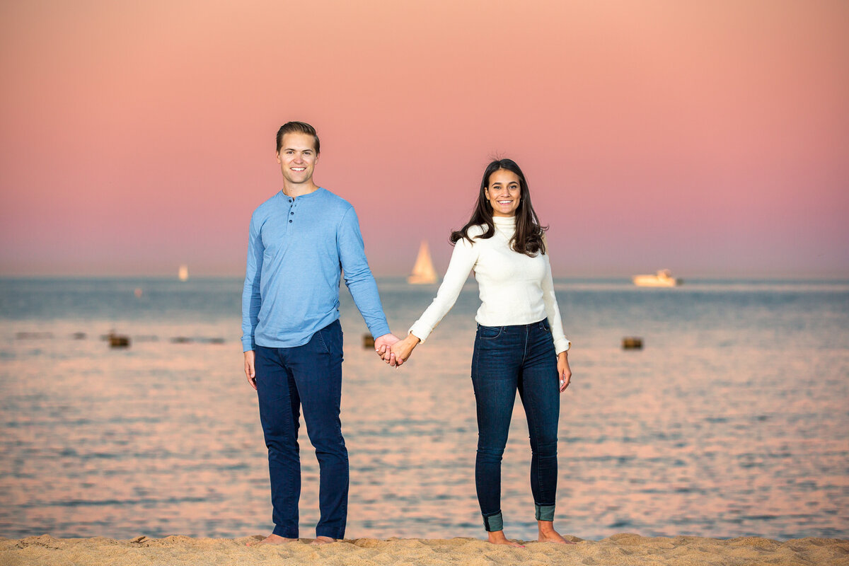 A couple wearing jeans holds hands on a Lake Michigan beach.