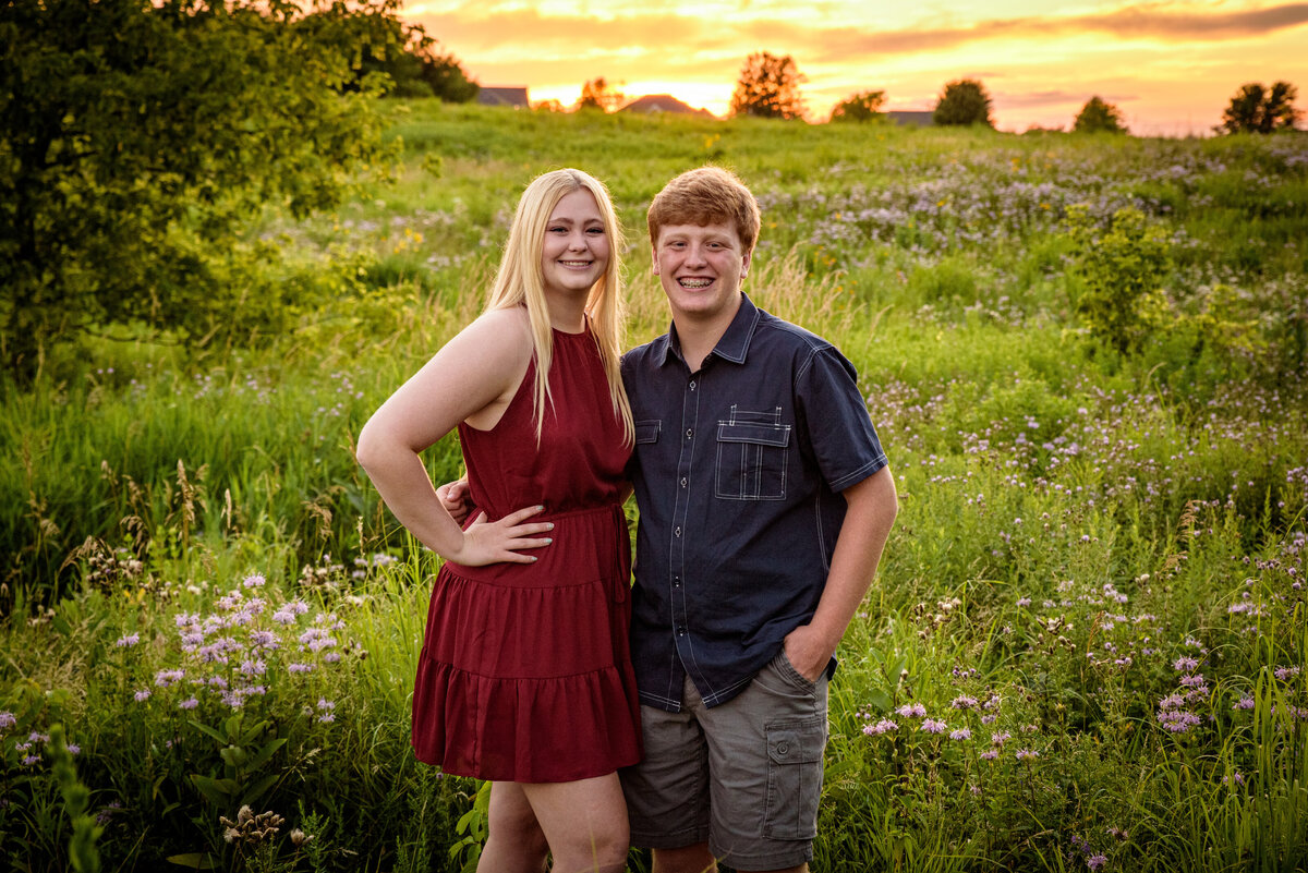 Sibling portrait of teenage brother and sister standing in long grassy field with a beautiful sunset at Fonferek Glen County Park near Green Bay, Wisconsin