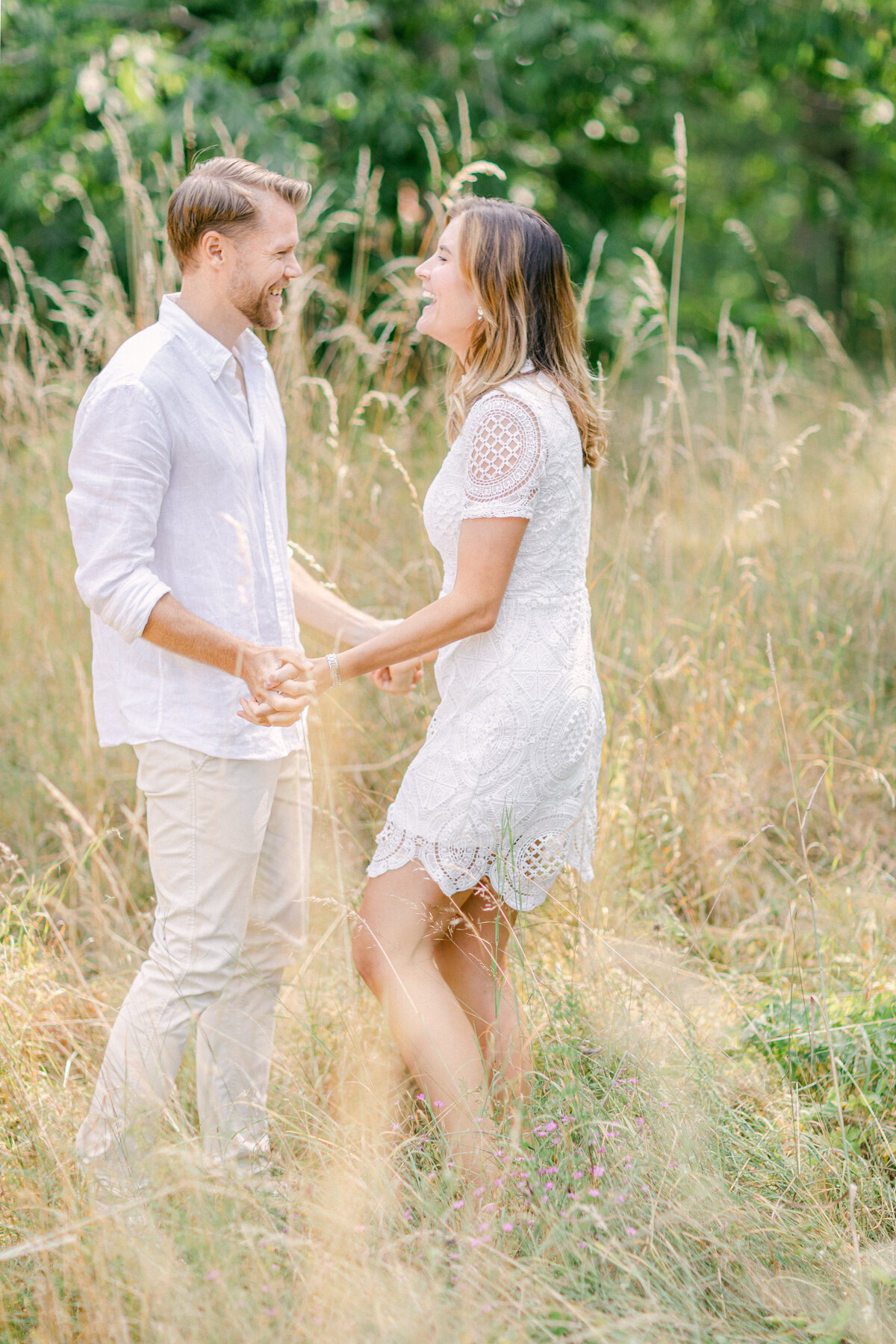 Par som håller varandra i händerna och skrattar i ett fält av torkat gräs