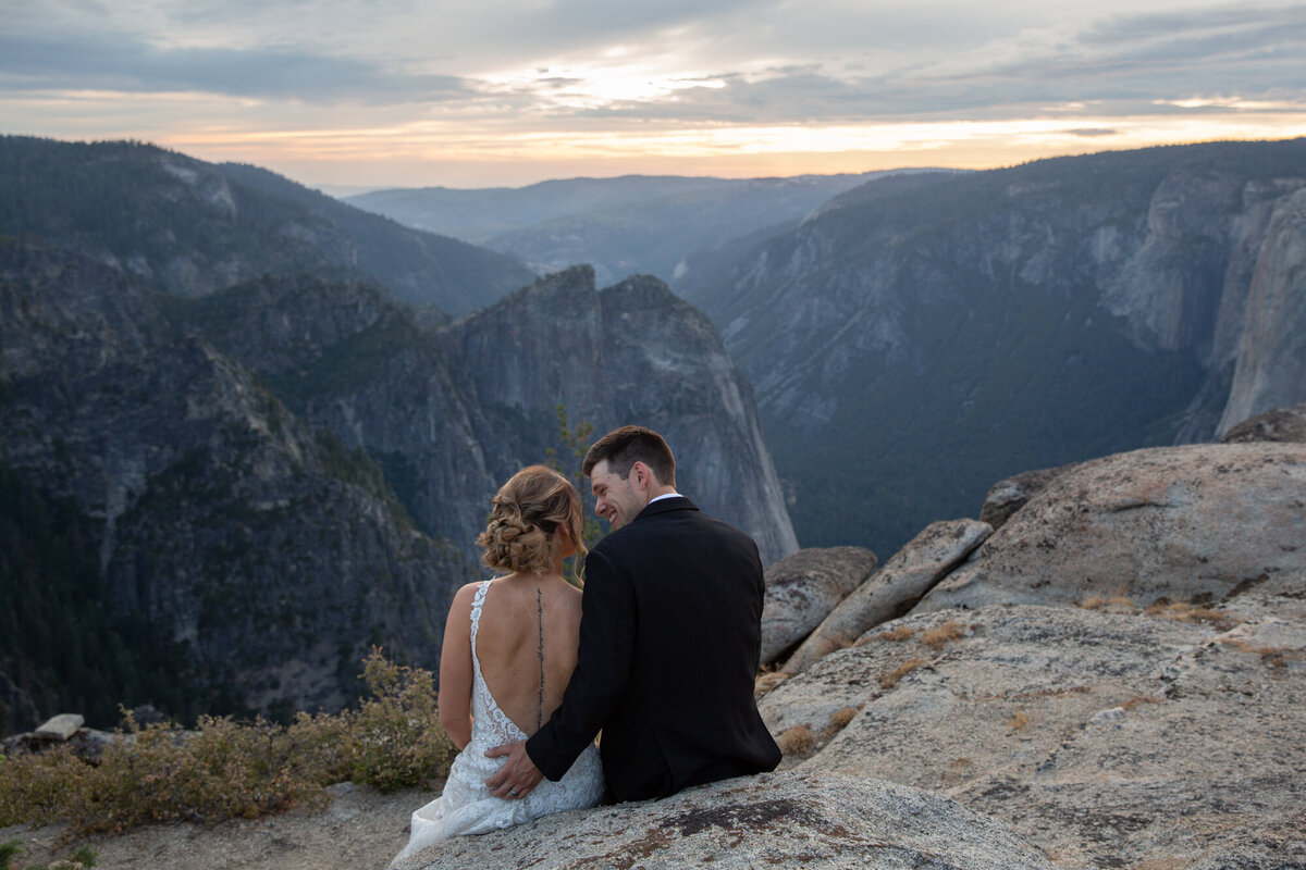 A bride and groom sit next to each other talking while they take in the beautiful mountain views in Yosemite.
