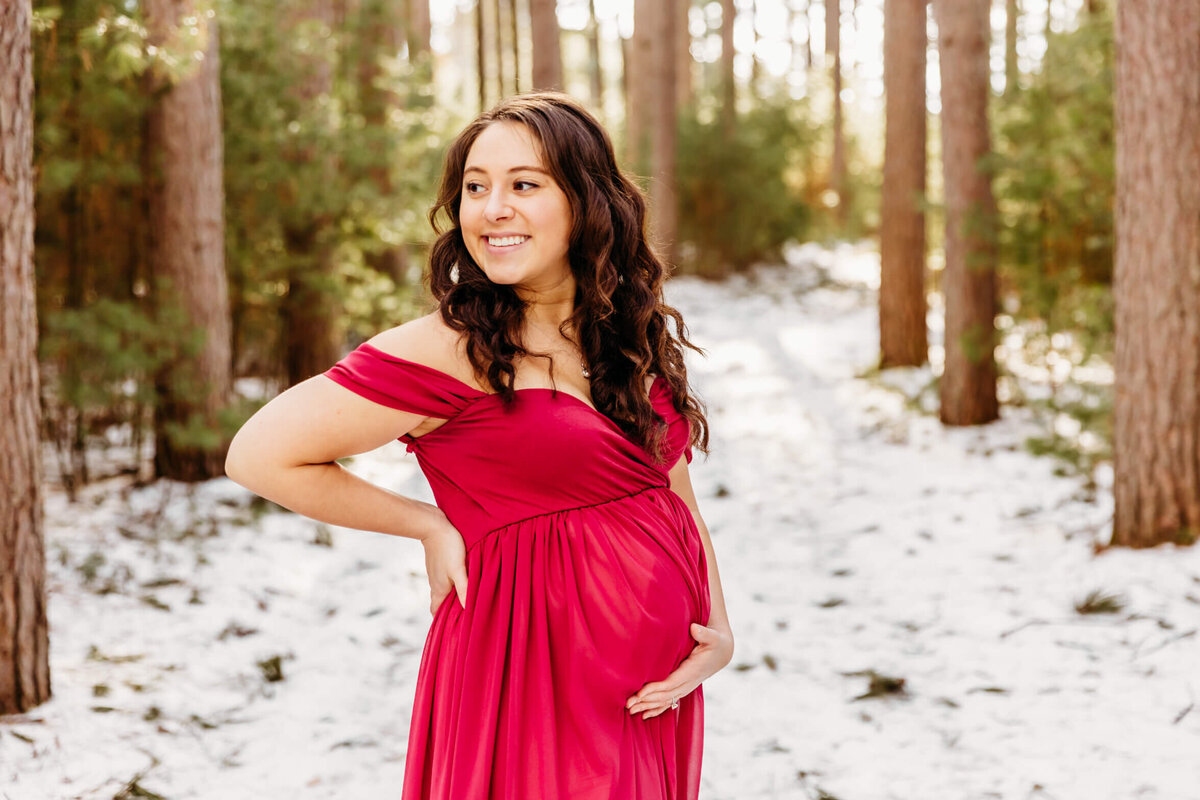 gorgeous pregnant mother posing in a snowy red pine forest for her maternity photography experience