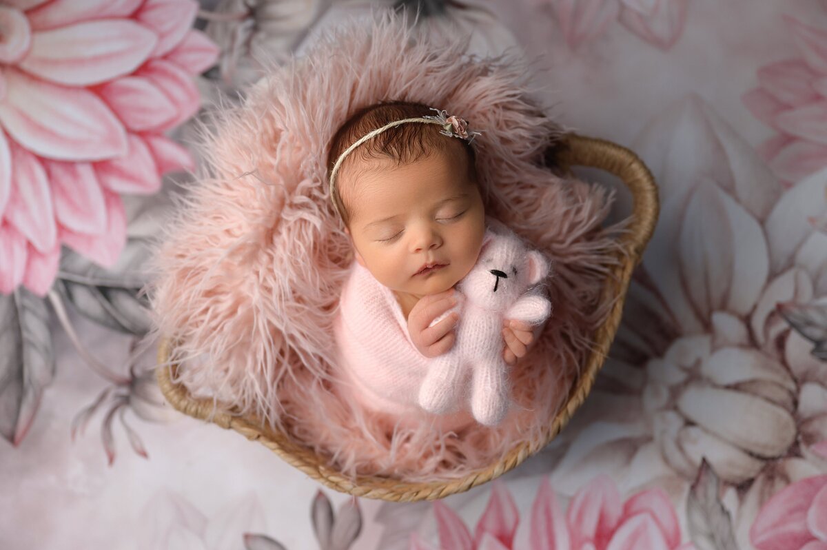 Newborn baby girl in floral theme with a teddy bear posed in a prop.