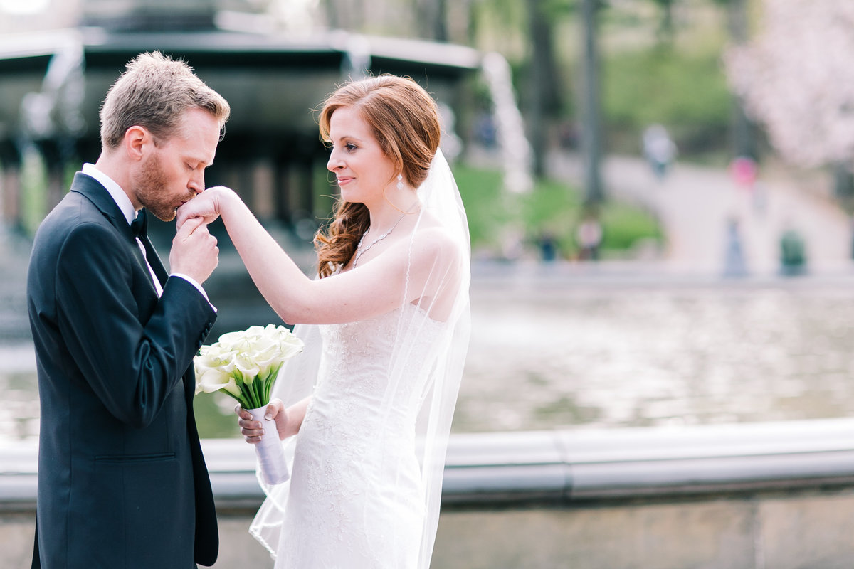 groom kissing his brides hand in central park