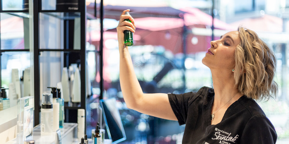 Ethetician standing at product counter while applying a spray to her face