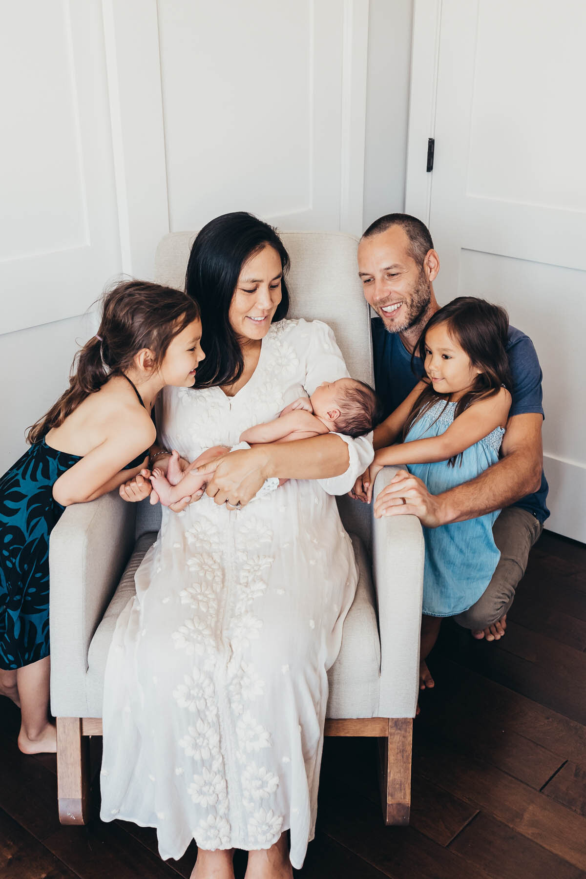 a family of five gather around mom sitting in a chair holding their newborn baby