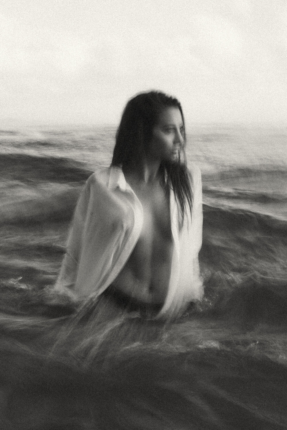 Slow motion blurred image of a model in the water wearing a white linen shirt