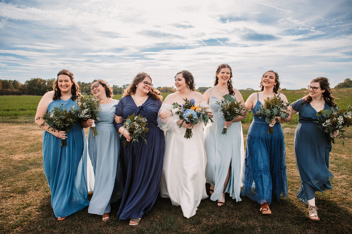 A bride walks in a field with her bridesmaids smiling at each other