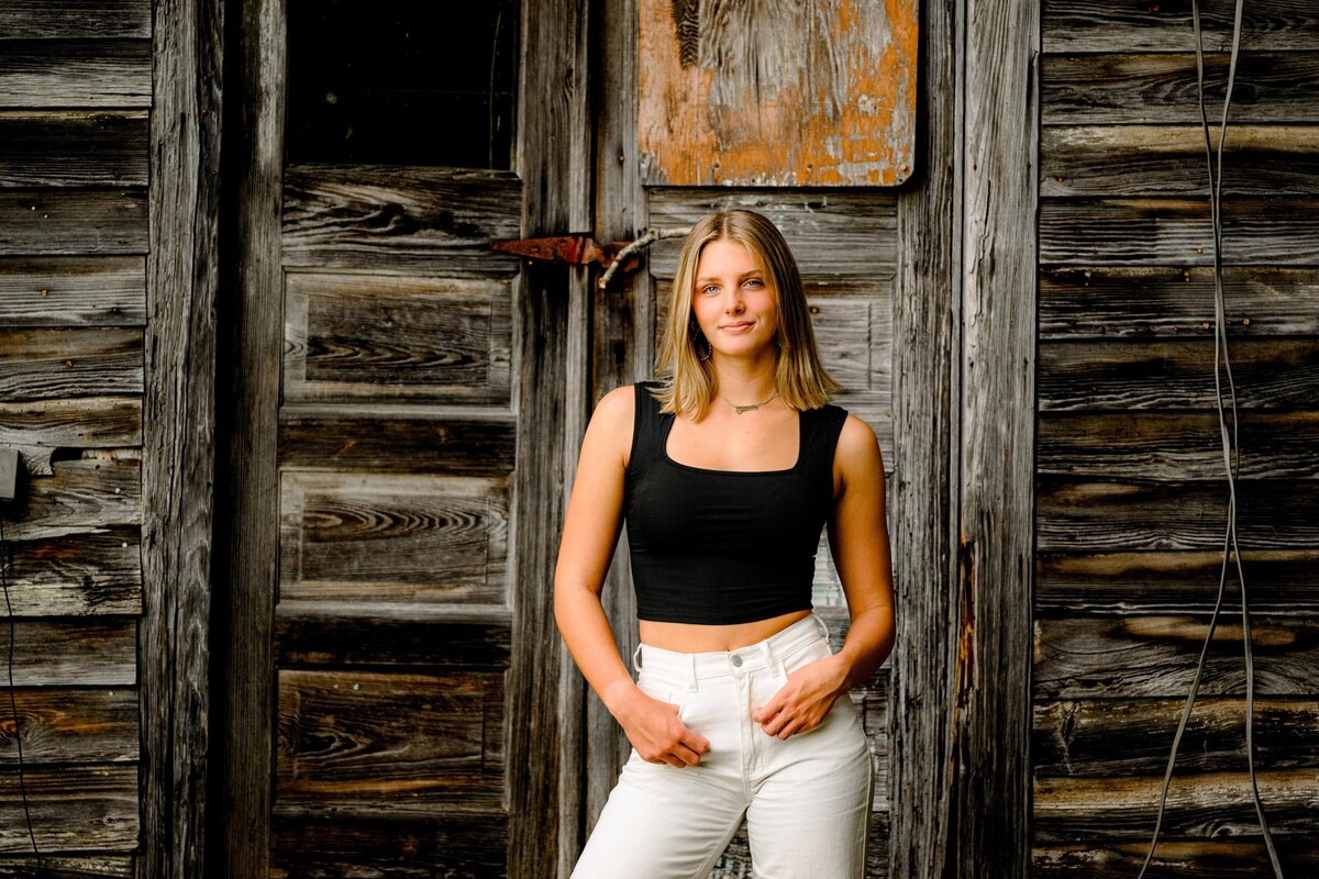 Senior in high school dressed in a black top and white jeans stanging in front of an old building