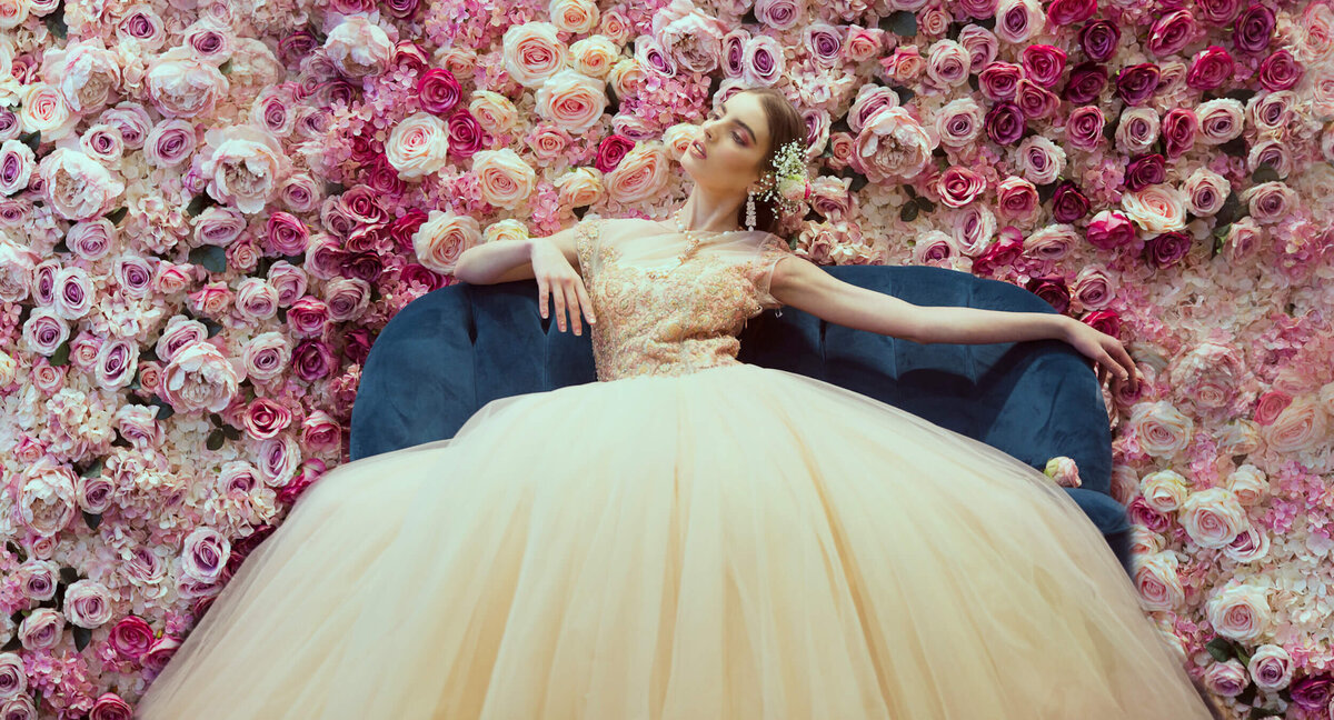 Beautiful lady in big dress sat on a sofa with a flower wall behind her