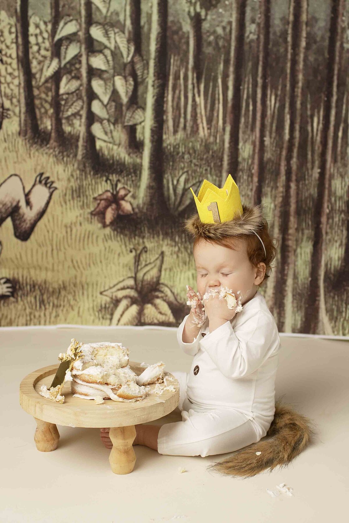 Redhead birthday boy in a Where the Wild Things Are themed outfit, gleefully smashing his birthday cake