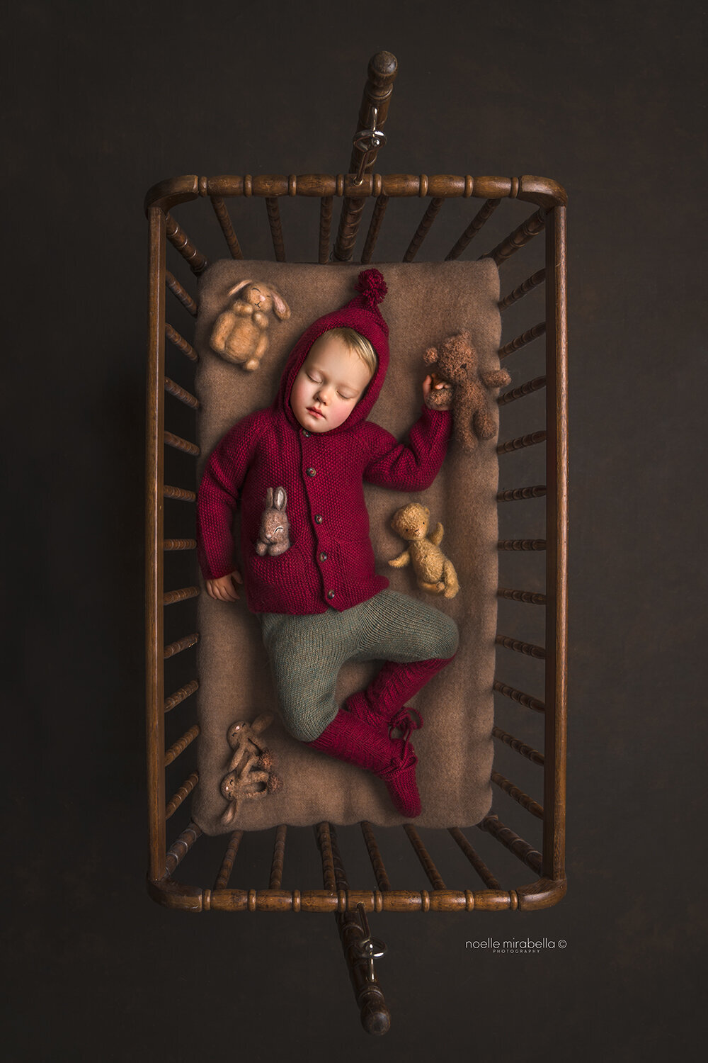 Baby wearing red and green hand knits sleeping in a Jenny Lind cradle.