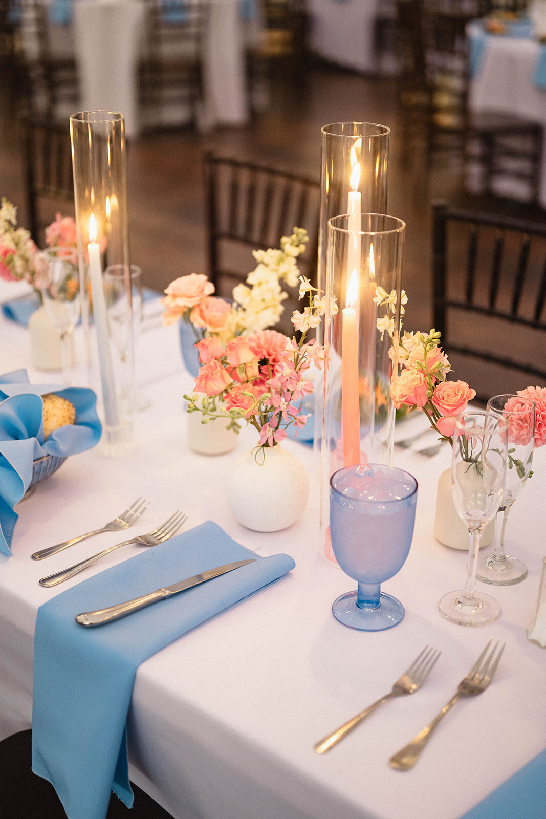 White wedding reception tables with blue napkins and pink florals