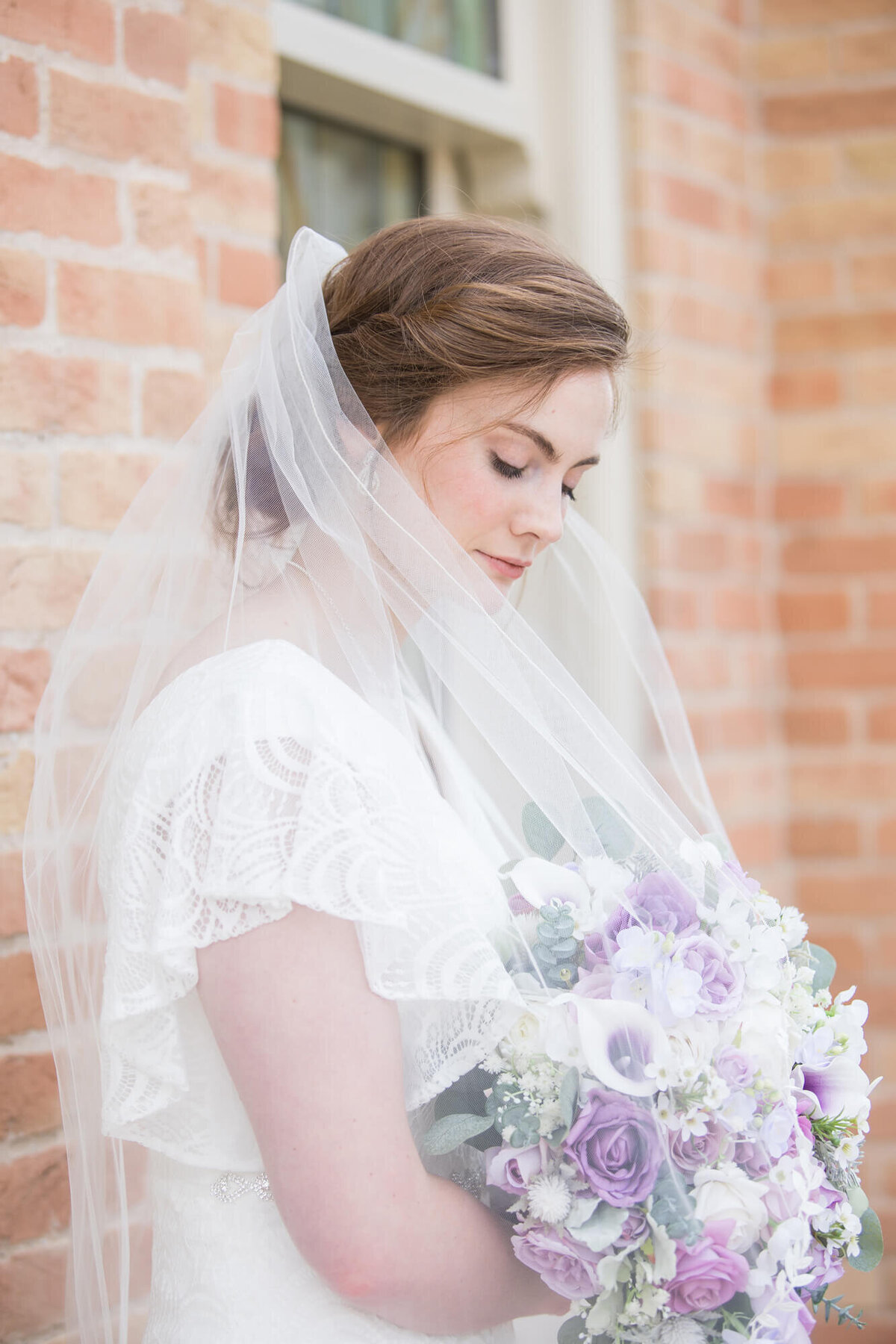 bride with a veil looking down at her purple rose bouquet