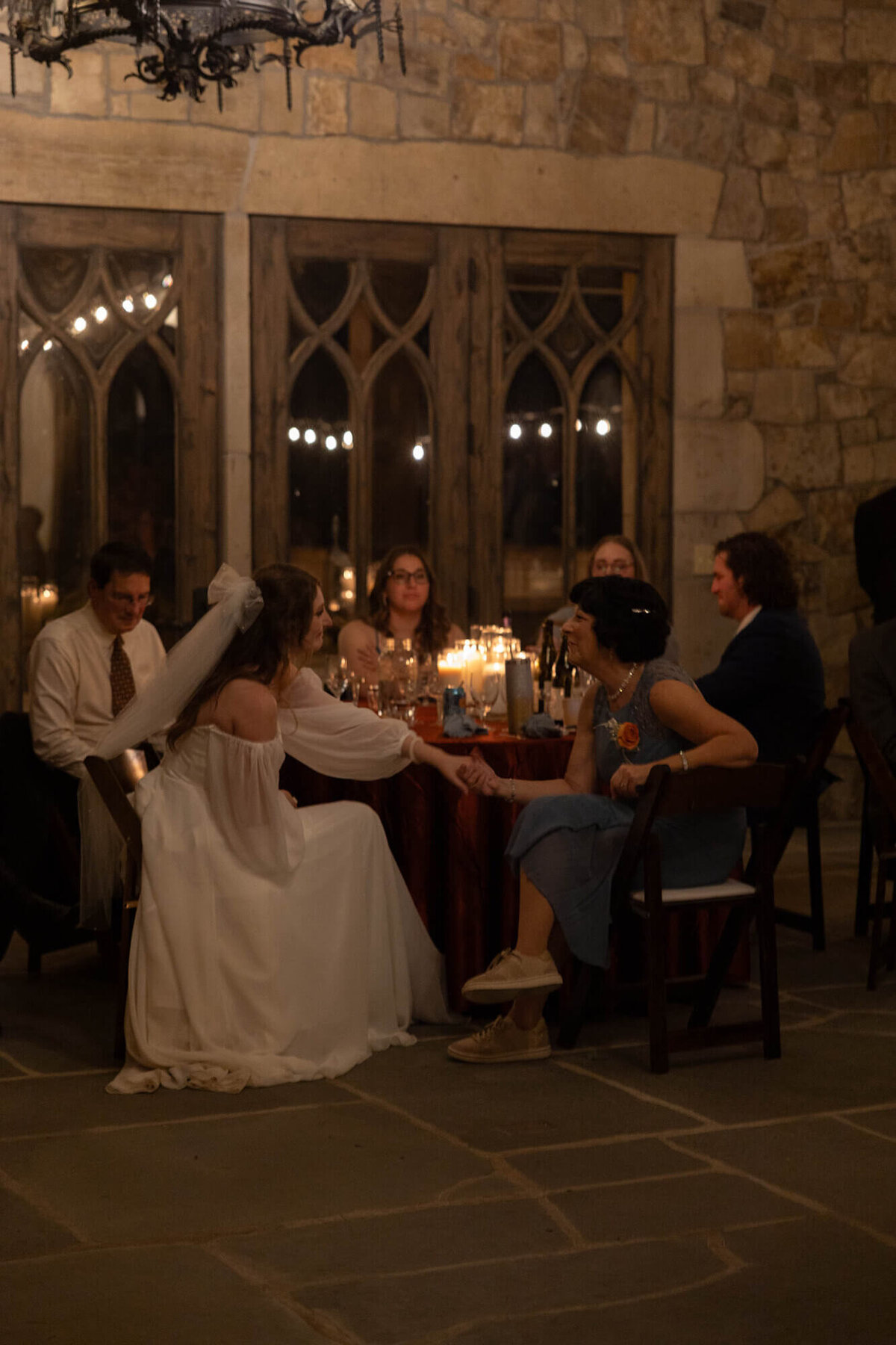 A woman holds hands with the bride seated at a table during indoor wedding reception at the Chateu de Lis.