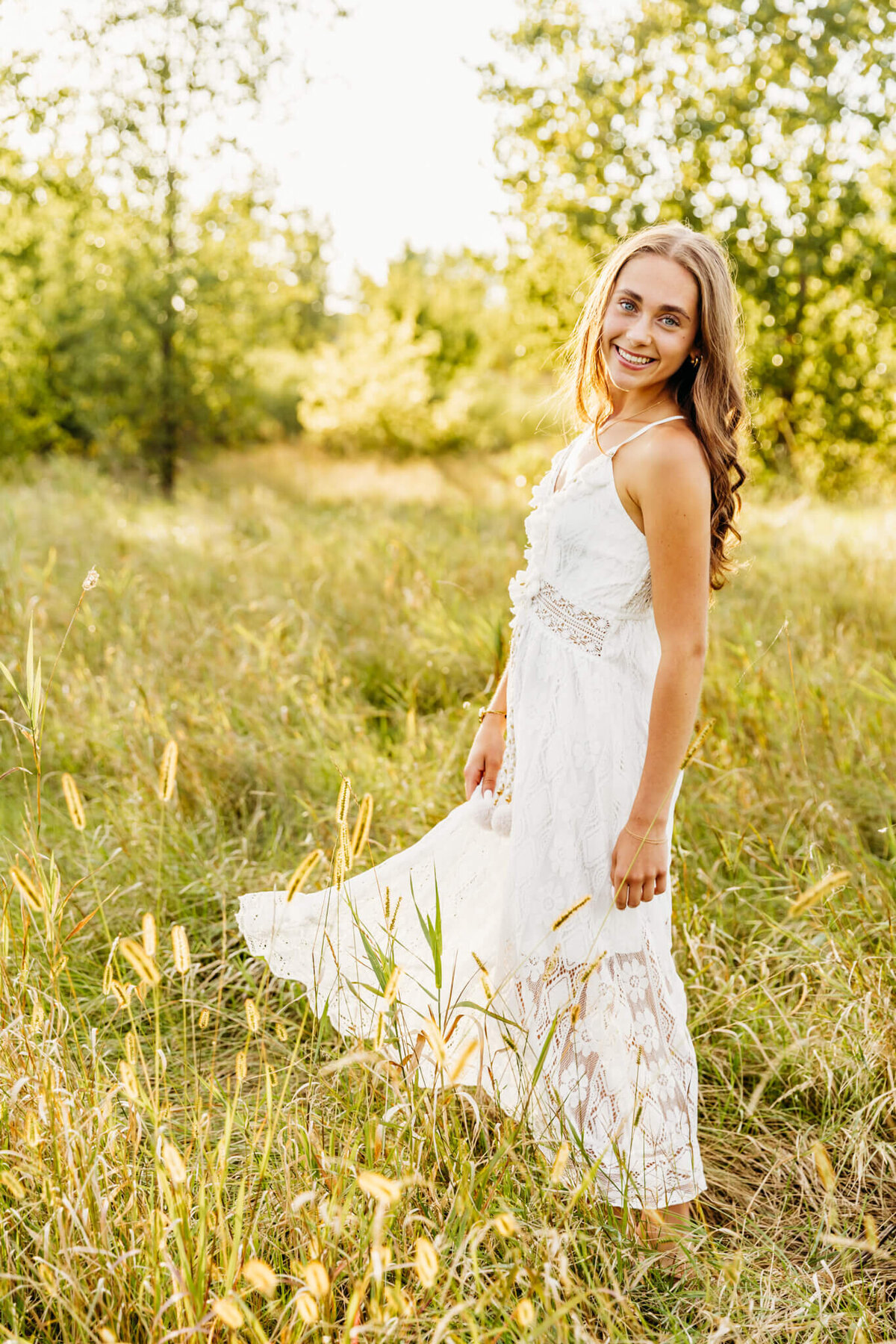 stunning young woman in a lace white dress twirling and smiling as she looks over her shoulder for her senior photography session