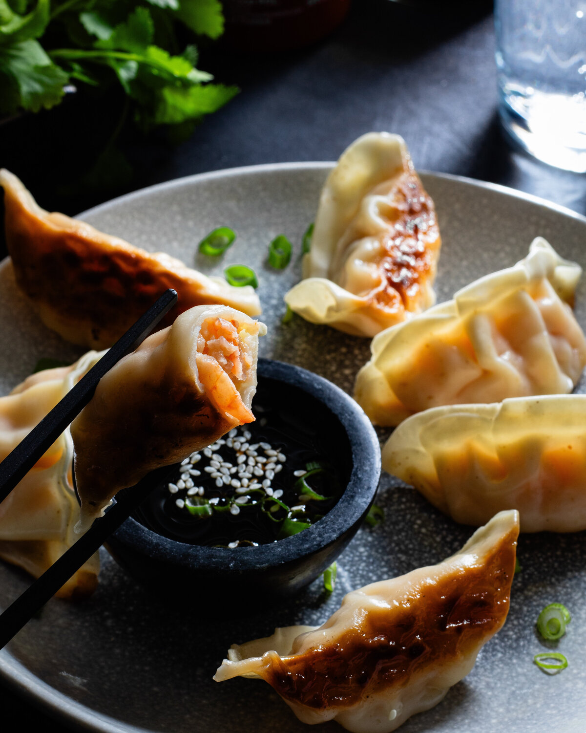 Shrip gyoza held with chopsticks over a soy sauce dip bowl