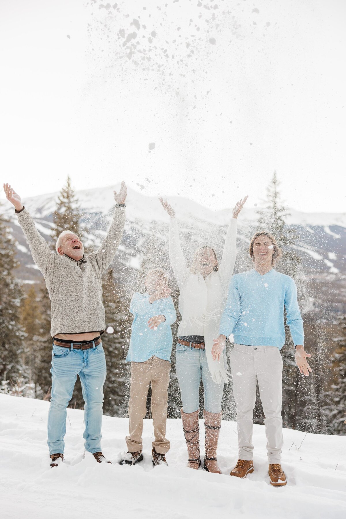 A happy family of 4 in blue throw snow up in the air on a mountain overlook