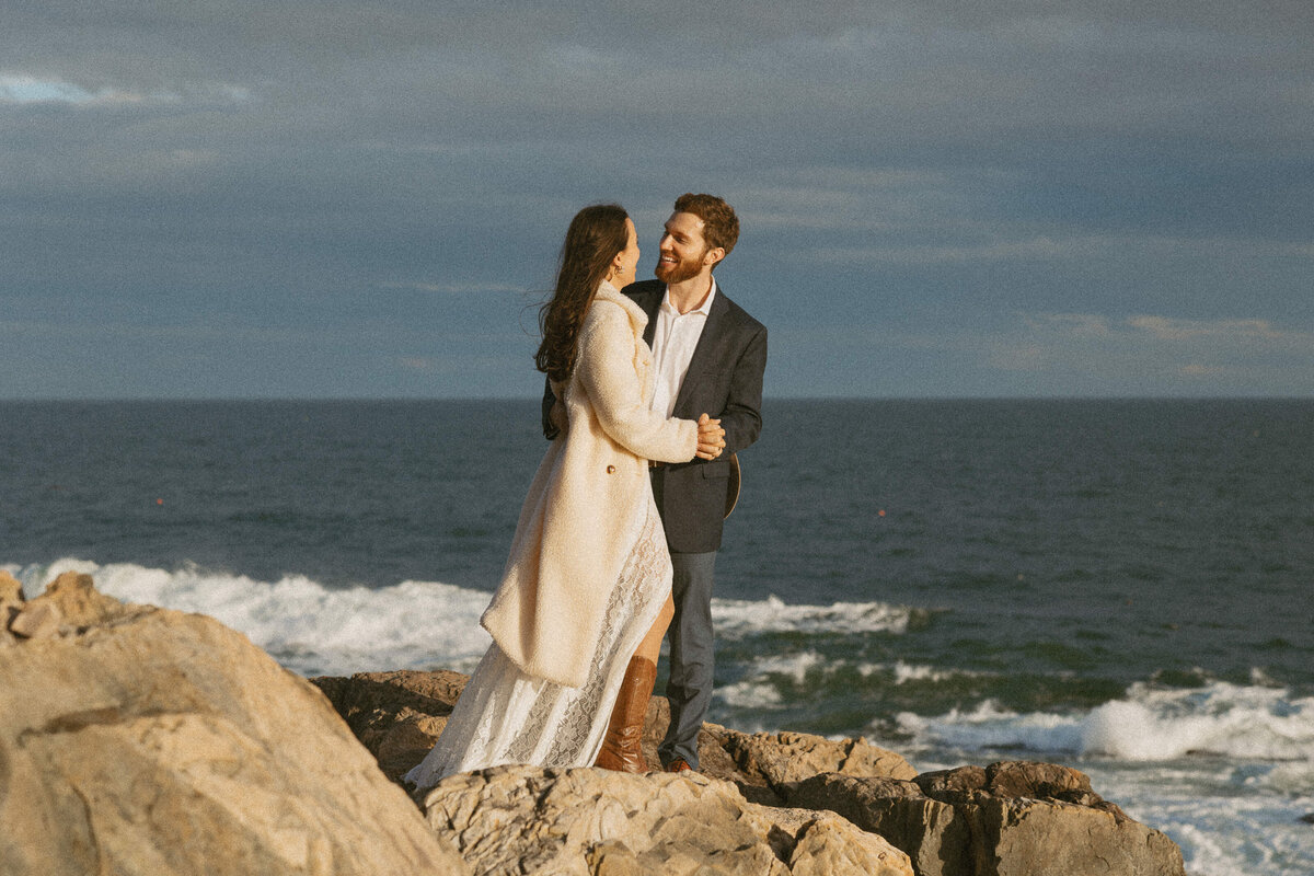 Couple standing on the edge of a rock laughing at their Acadia Adventure Wedding