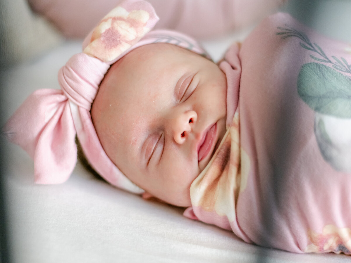 Newborn baby with pink floral headband and wrap laying in her Richdmond crib.