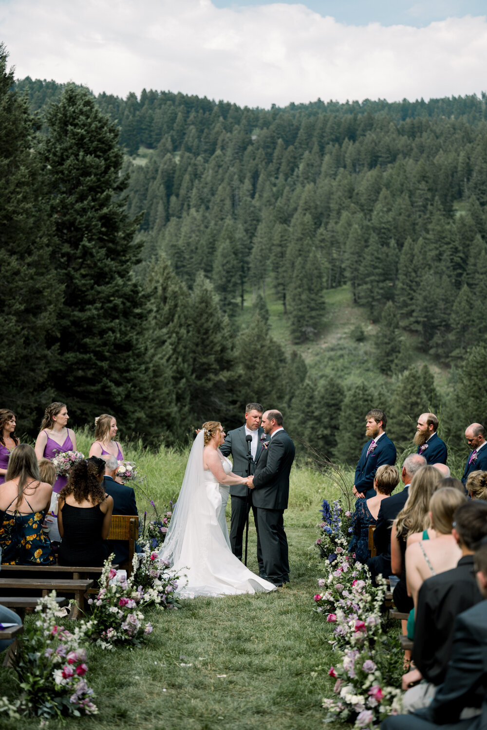 Bride and groom exchanging vows at their outdoor Montana wedding ceremony, surrounded by lush greenery and floral arrangements