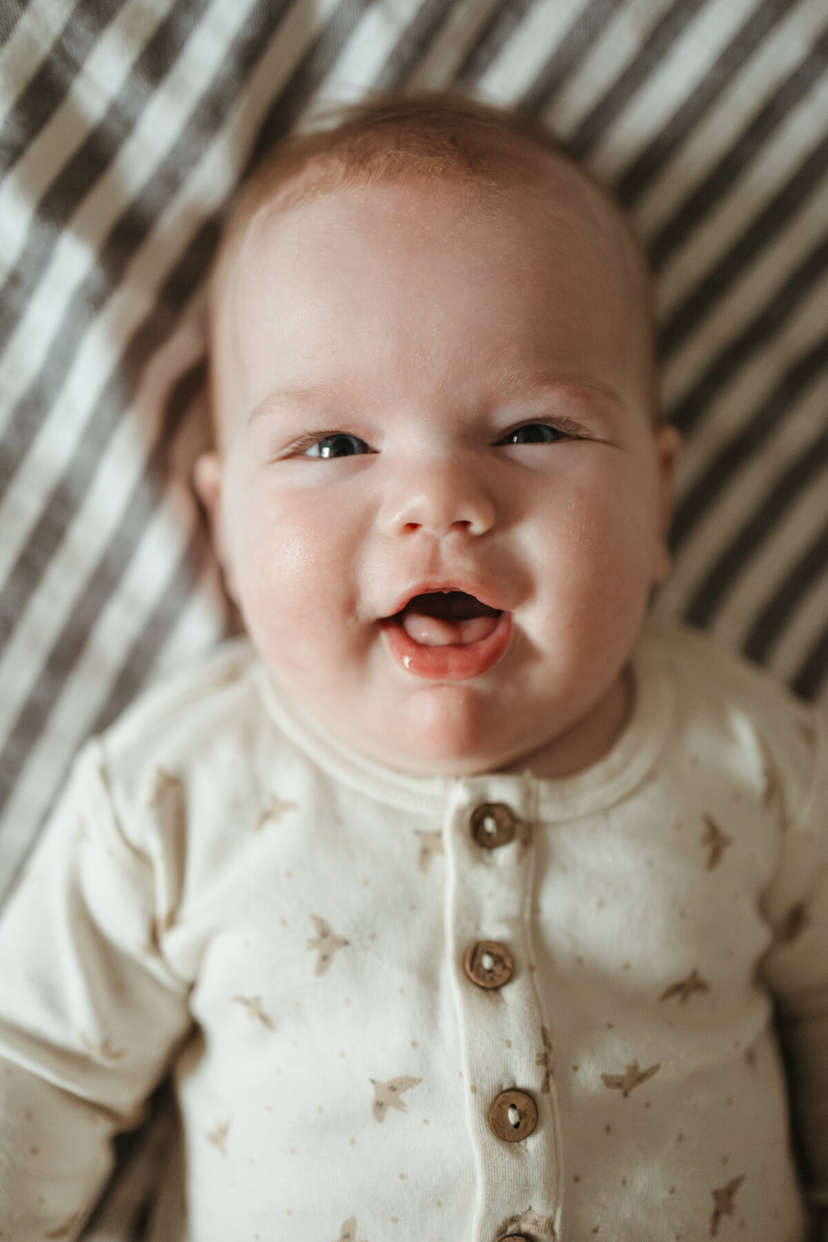 baby in white onesie looking up at camera with big smile during lifestyle in home family session with alexis adkins photography in longmont colorado