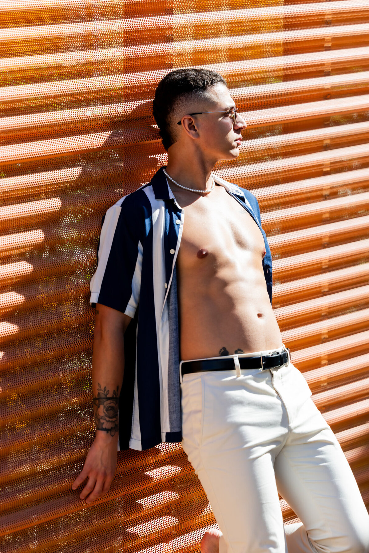 Individual standing against a slatted wood wall in Palm Springs, dressed in neutral tones with a modern editorial pose.