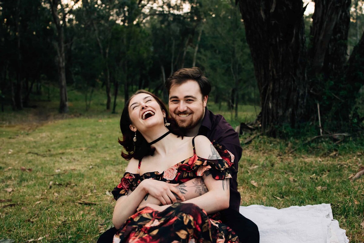 Woman with head back laughing with boyfriend, sitting on rug outside during couple photoshoot Melbourne, And So I Don't Forget Photography