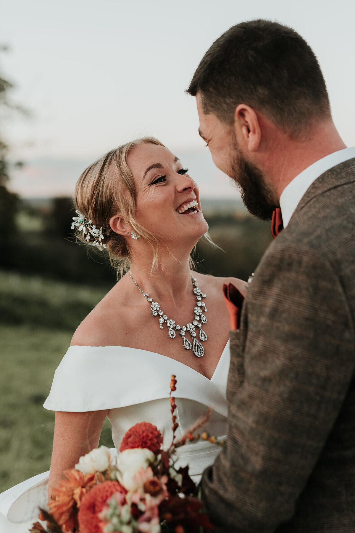 Bride smiling gently at her husband wearing stunning jewelled necklace at their Autumn wedding at Montague Farm, Sussex