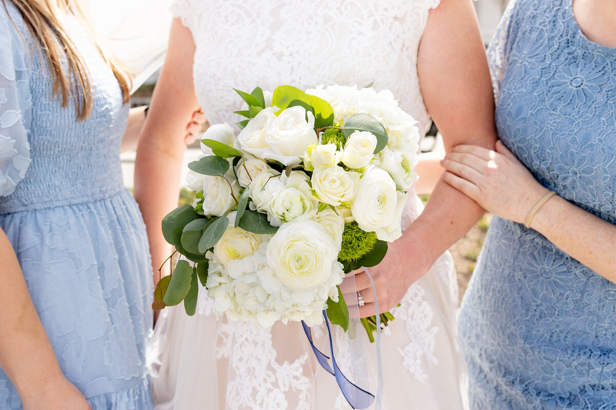 A detailed view of the bride's bouquet, showcasing white roses, ranunculus, and lush greenery held against her lace dress.