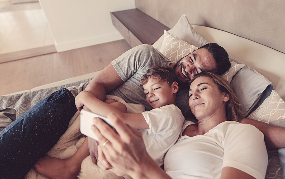 A family of three smiles as they lay in bed. This could symbolize a thriving relationship. We offer infidelity recovery in Florida. Contact us for support with recovering from an affiar, and how to apologize for cheating.