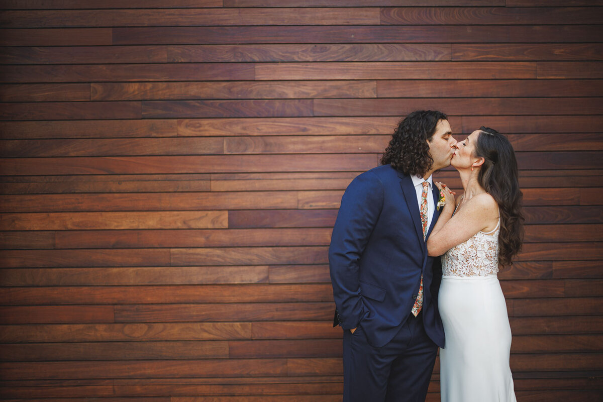 Bride and groom kiss near at the wooden wall