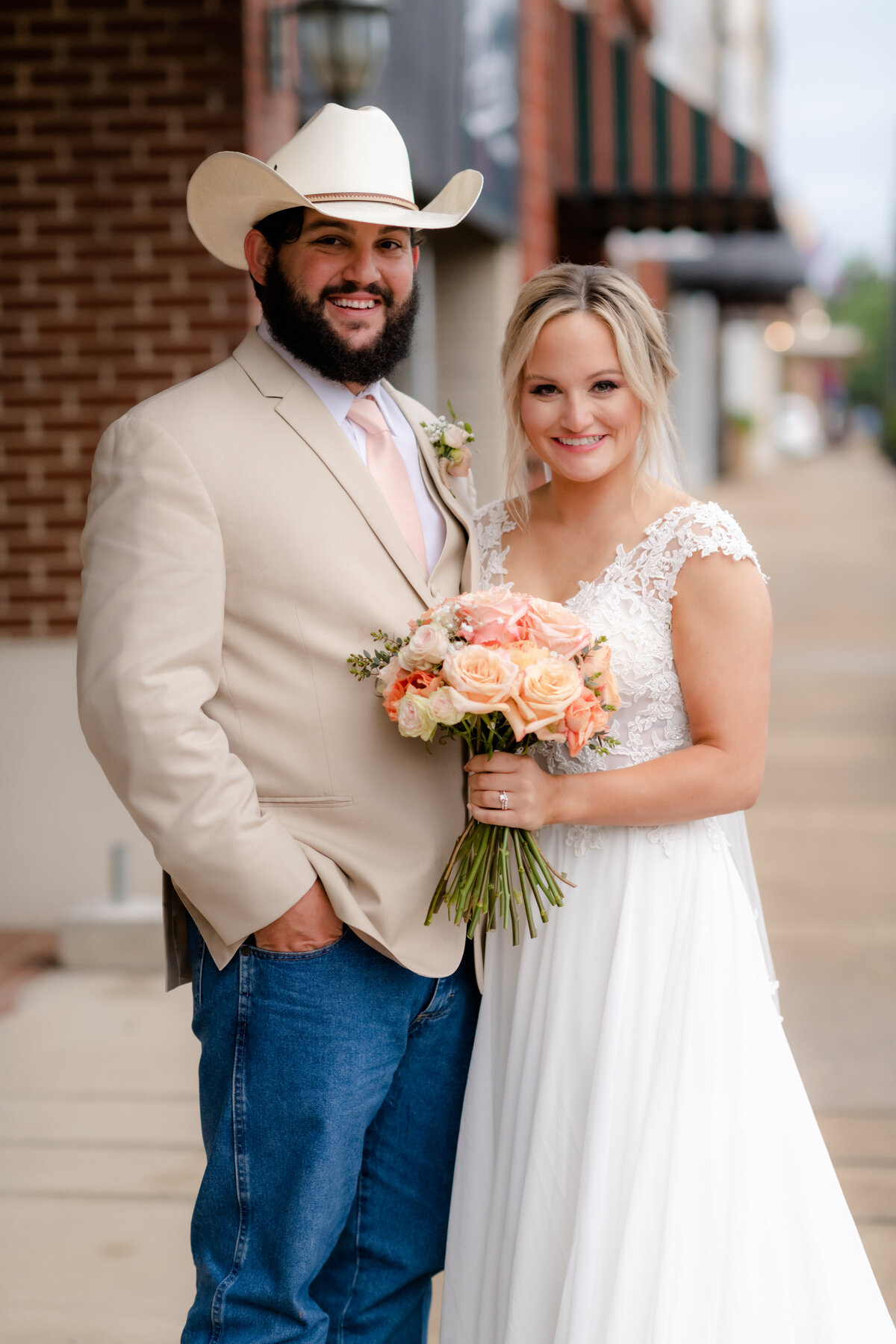 bride and groom standing on a sidewalk in downtown as they smiles at the Little Rock wedding photographer