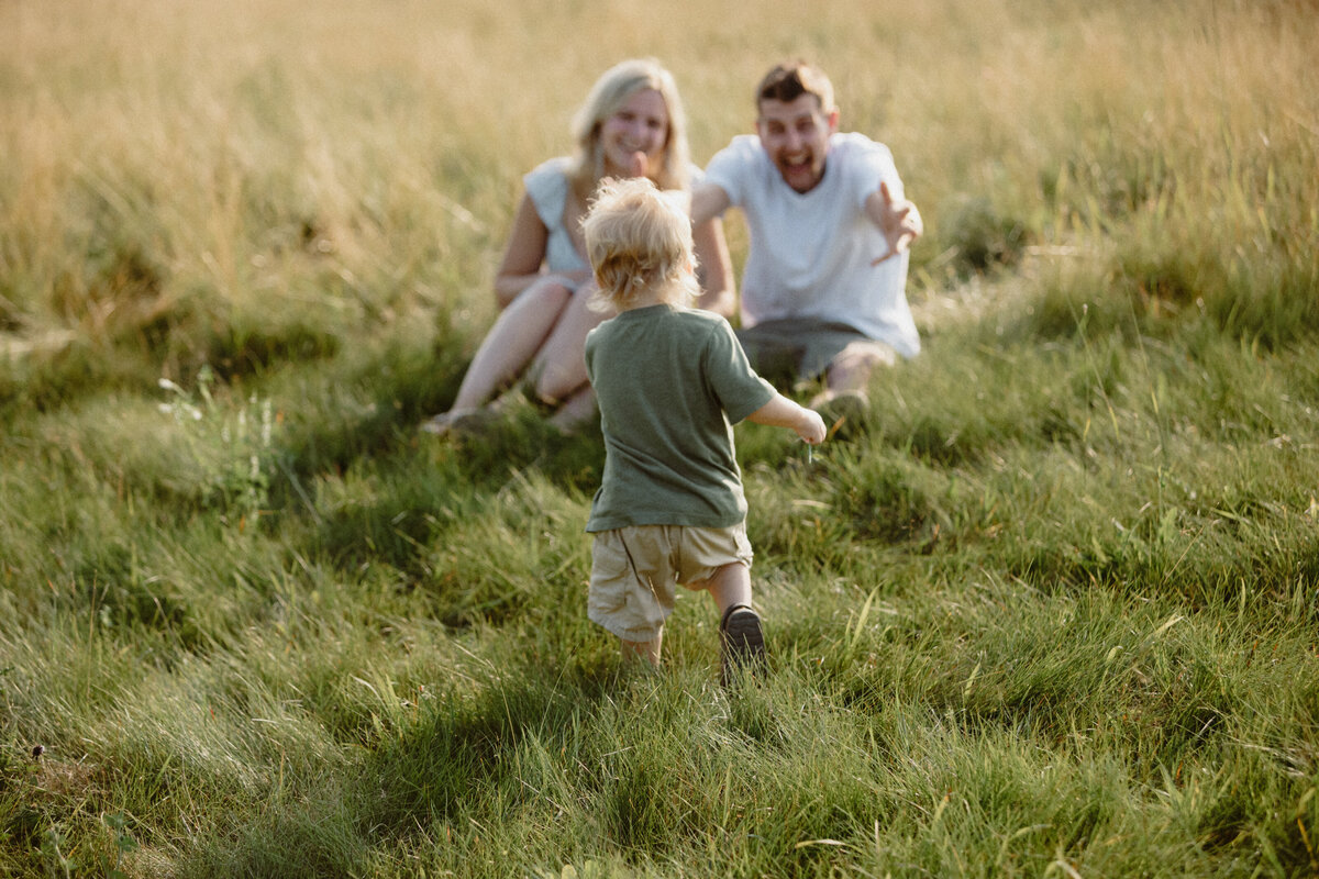little boy running towards his parents in a field