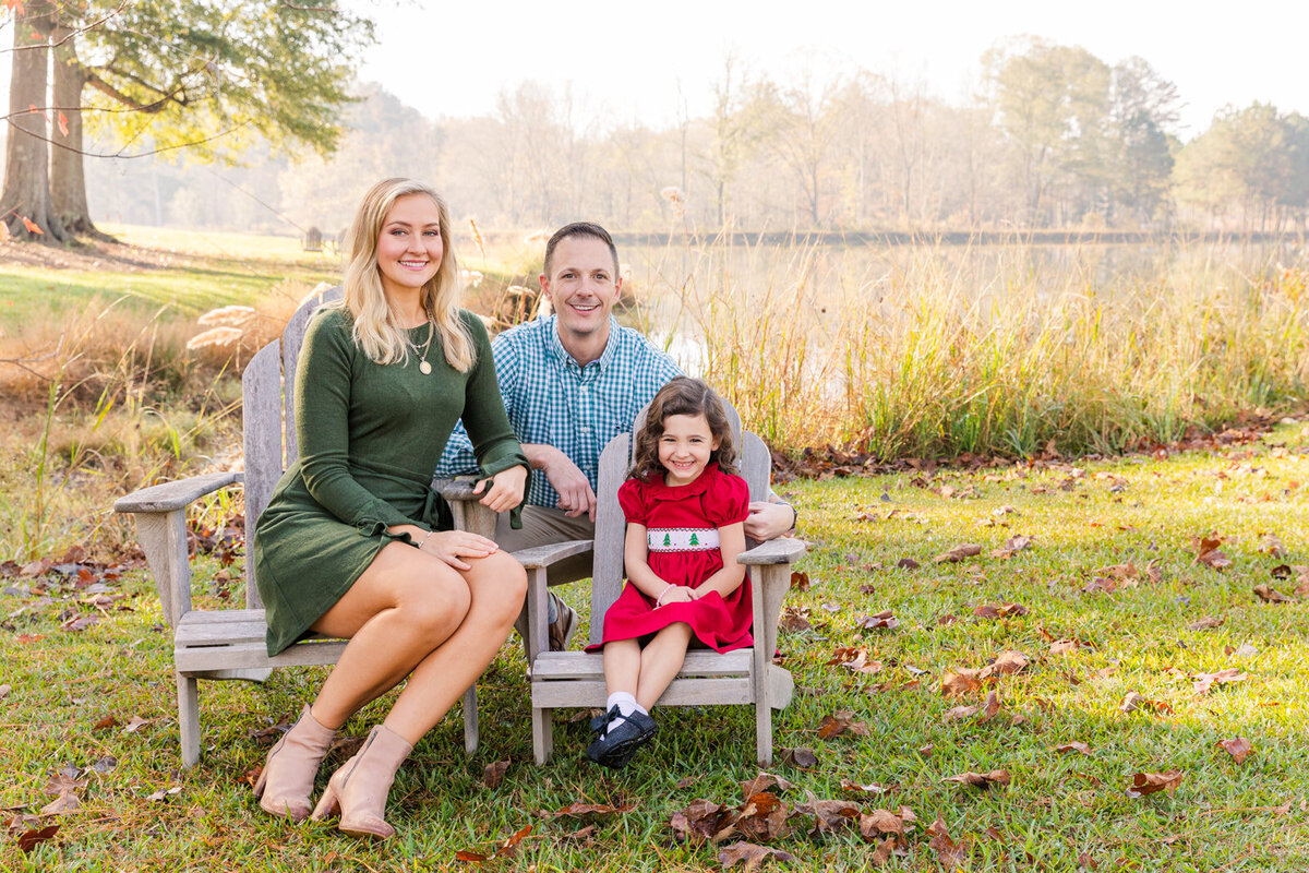 family with toddler daughter sitting on adirondack chairs near a pond in GA