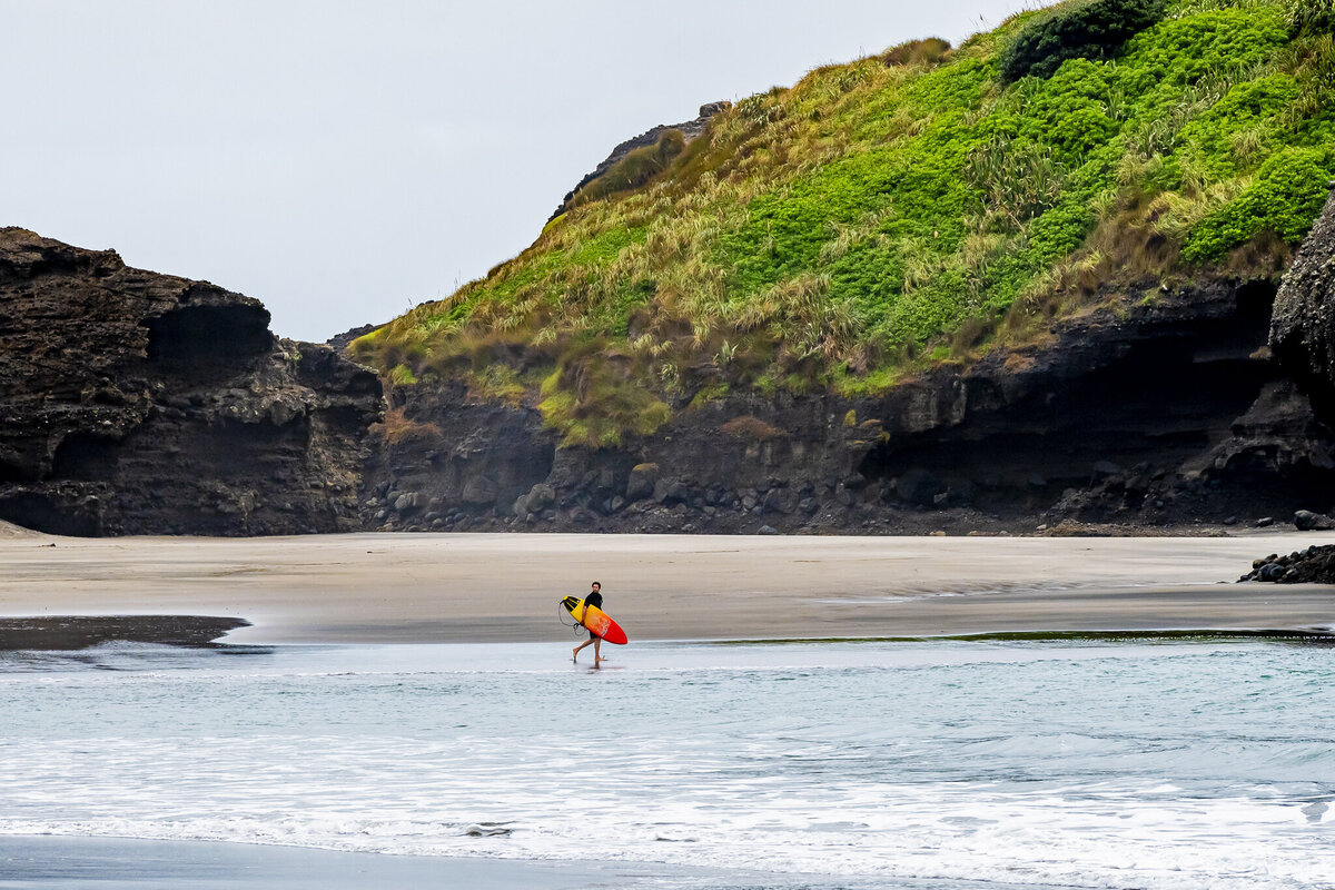 A surfer heads into the water at Piha beach, New Zealand.