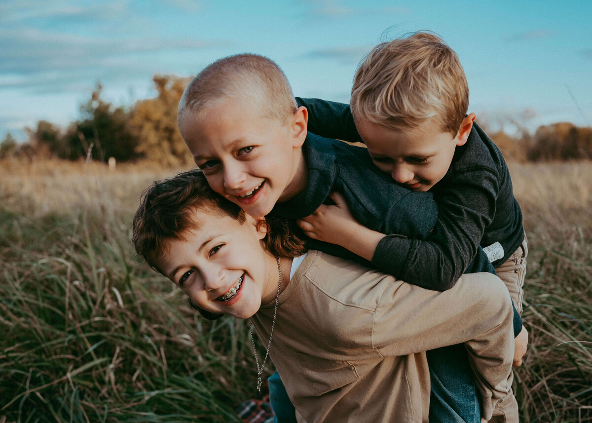 Three Wild brothers all pile onto each other's backs, and laughed towards the camera during a golden hour sunset session on their family farm.