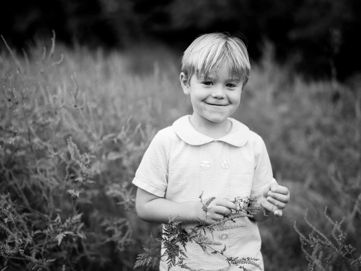 A small child smiling and holding a branch.