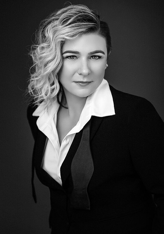 Black and white transformation portrait of a woman in a sharp suit with curled hair, exuding confidence and elegance.