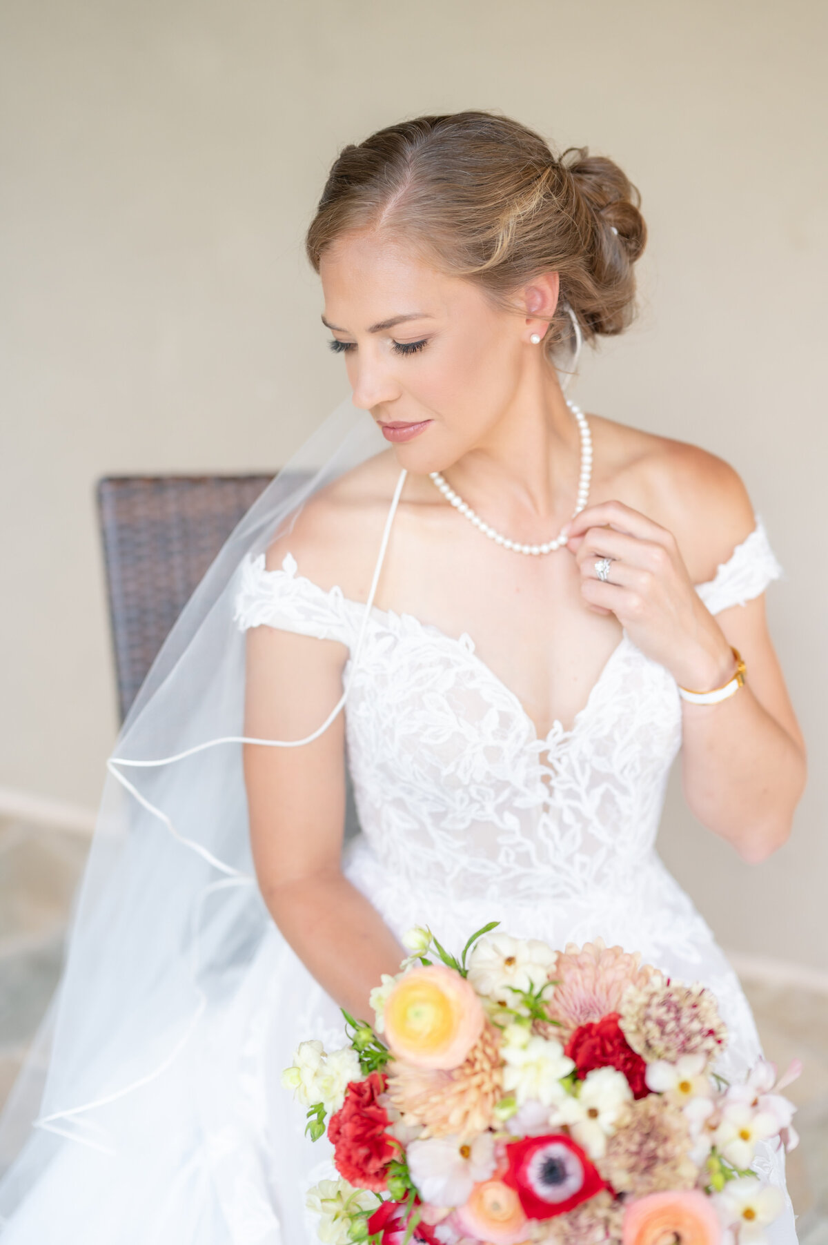 Colorado Springs bride smiling down over her shoulder while holding her pearl necklace 