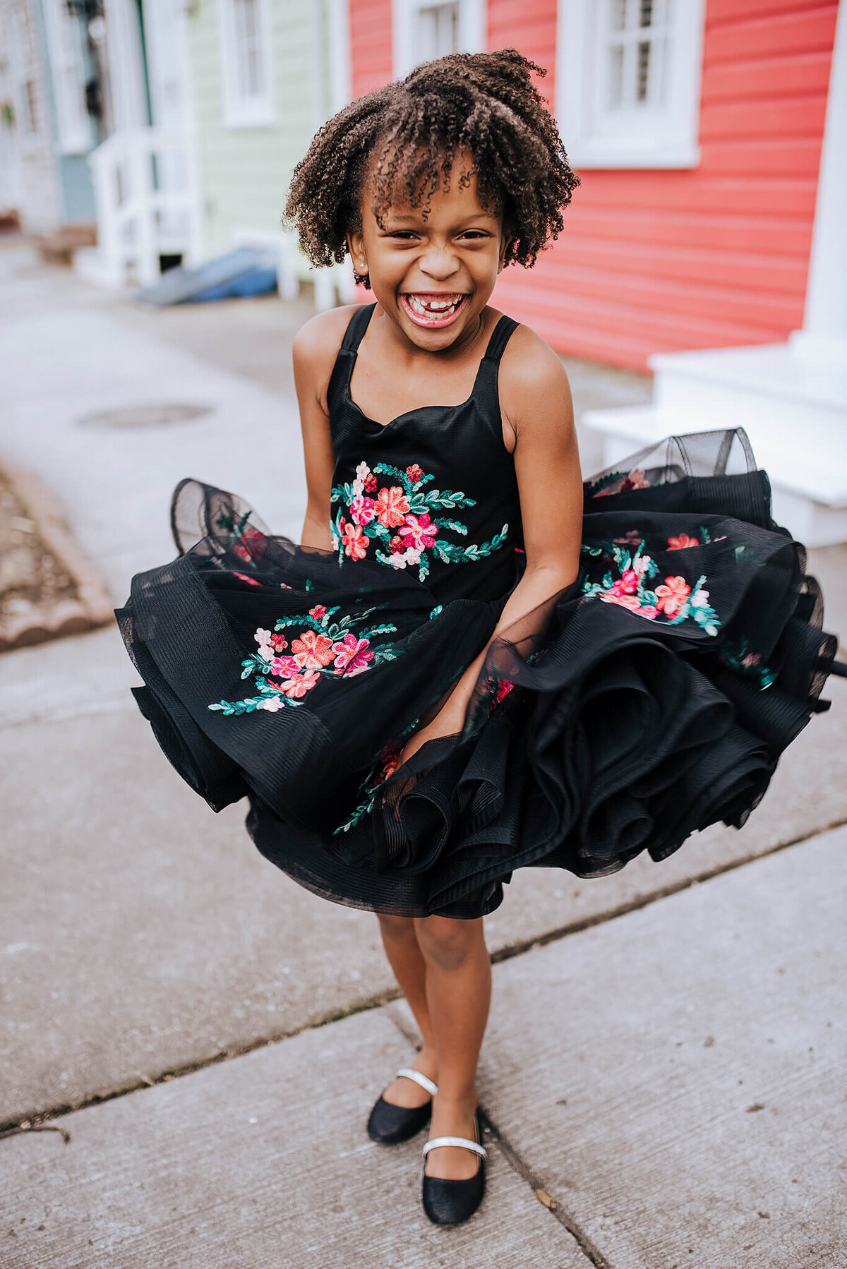 African American girl wearing black shoes and a black floral dress spinning and laughing in Fells Point Baltimore Maryland
