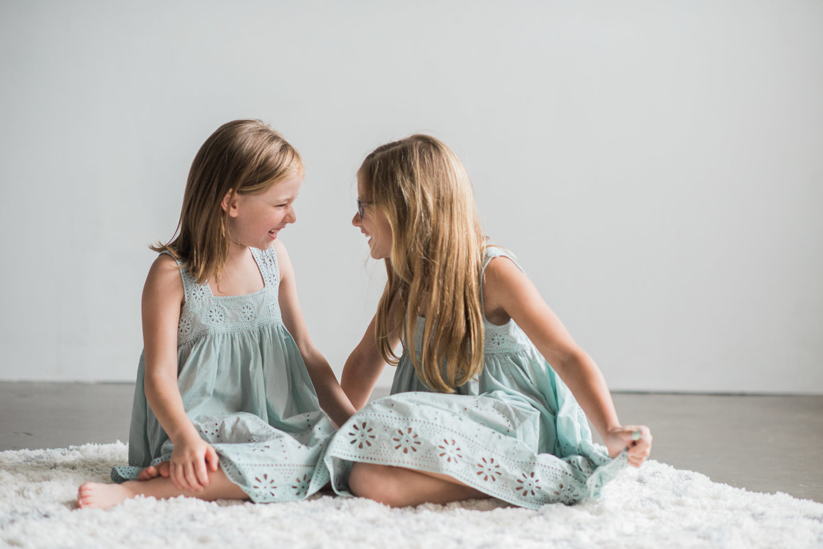 sisters in aqua dress on white rug laughing