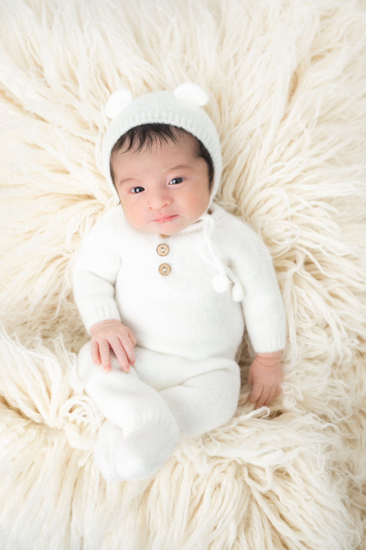 Smiling newborn dressed as a teddy bear, laying on plush off white flokati.